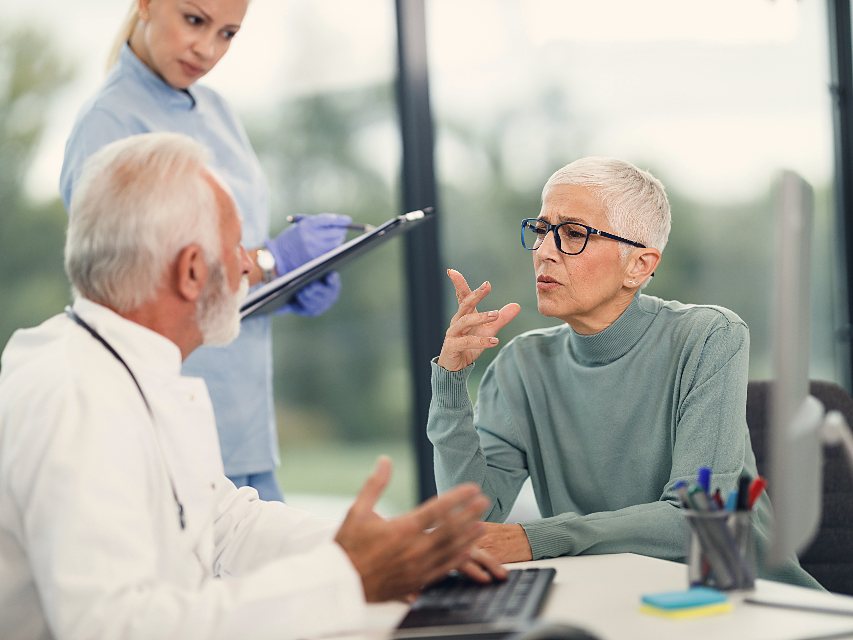 Un médico conversa con una paciente en su consultorio mientras revisa su historia.