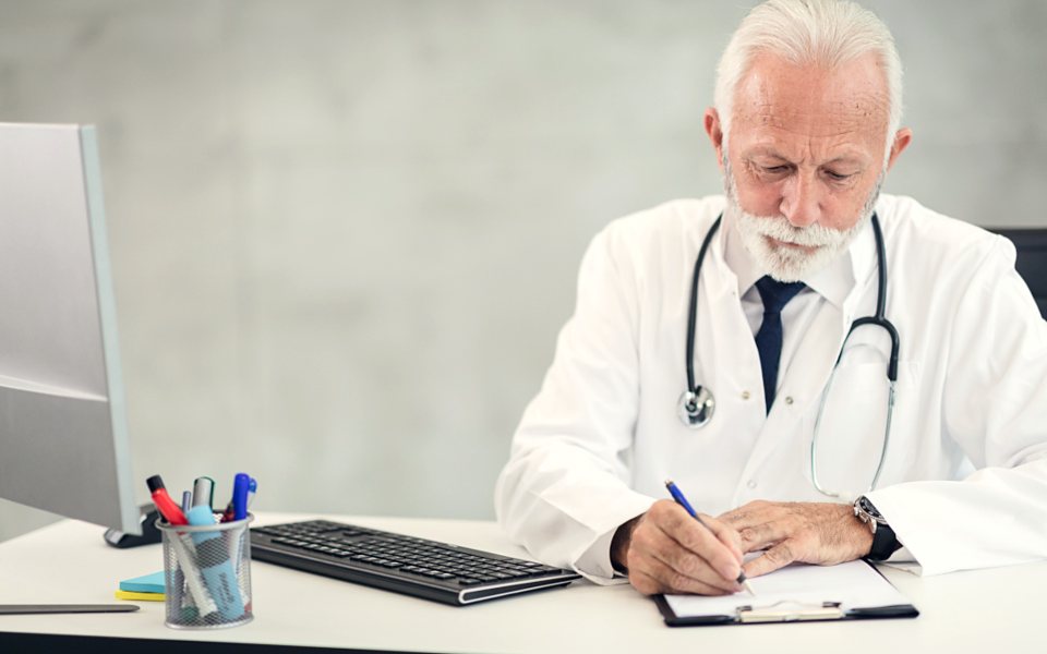 Médico revisando y anotando la historia de un paciente en su consultorio.